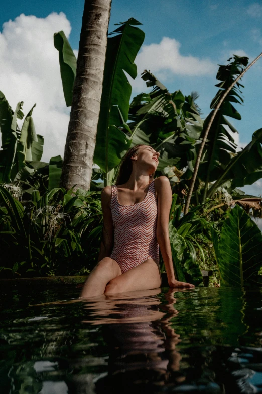 a woman in a one piece swimsuit sitting in the middle of a palm forest