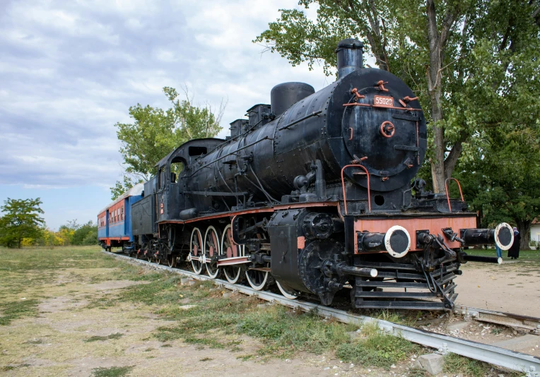 an old steam locomotive with several cars on tracks in a field