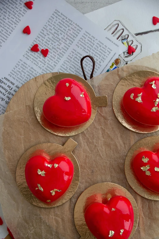 four cupcakes with red icing and hearts are placed on a brown plate with other decorations