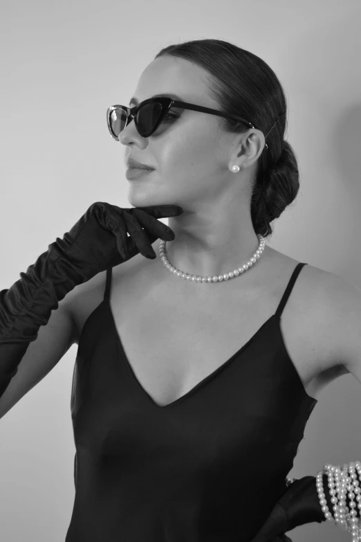 a woman wearing gloves and pearls stands in a white room