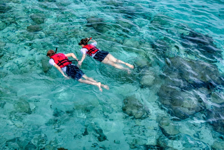 two people in life jackets are floating on some clear water