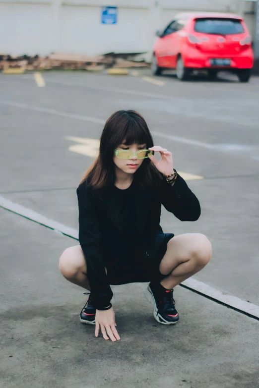 a woman is kneeling down wearing a black shirt and a pair of yellow sunglasses