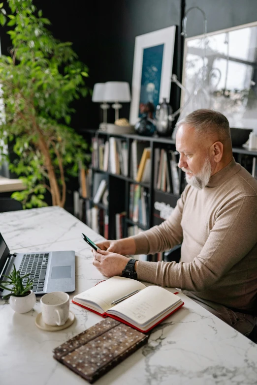 a man sits at a table in a liry, with his laptop, notebook and books