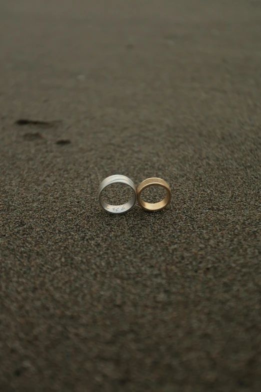 two wedding rings laying on the sand near a footprints