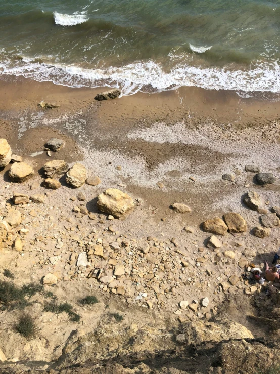 two people are sitting at the edge of the water and looking out to the beach