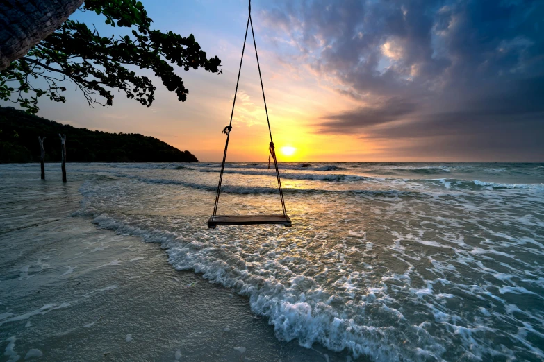 swings that are placed on the shore near a sunset