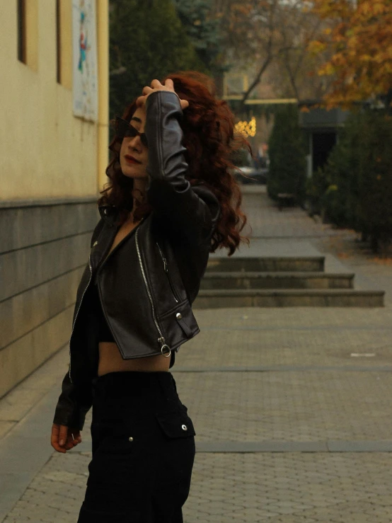 a woman in leather jacket walking on sidewalk next to building