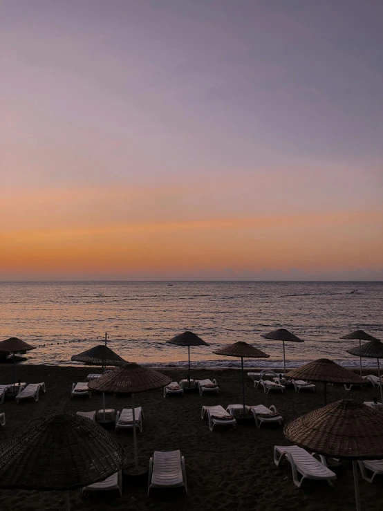 a sunset at an empty beach with chairs and umbrellas