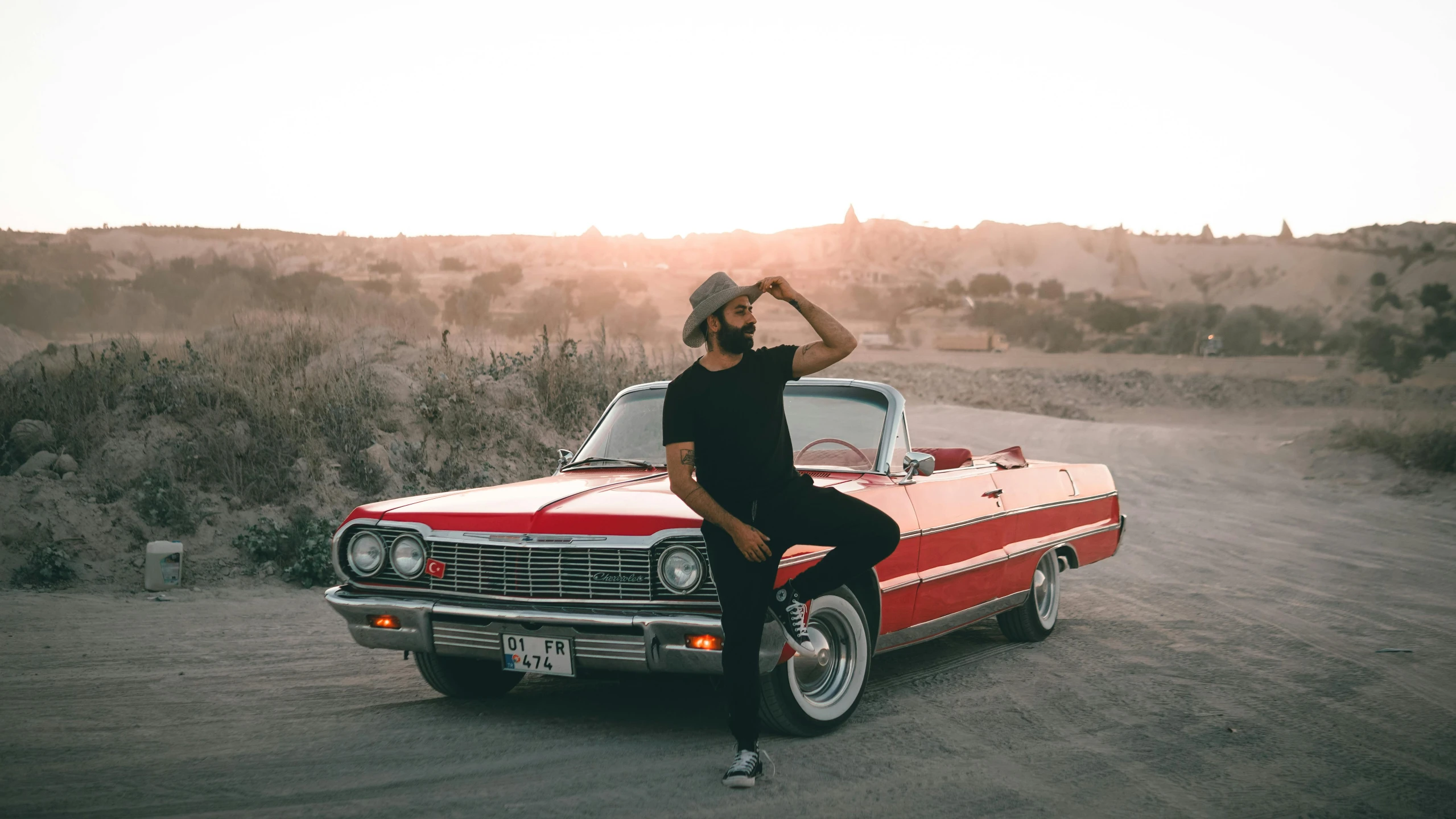 an old school car with a man on the hood and a hat on standing by it