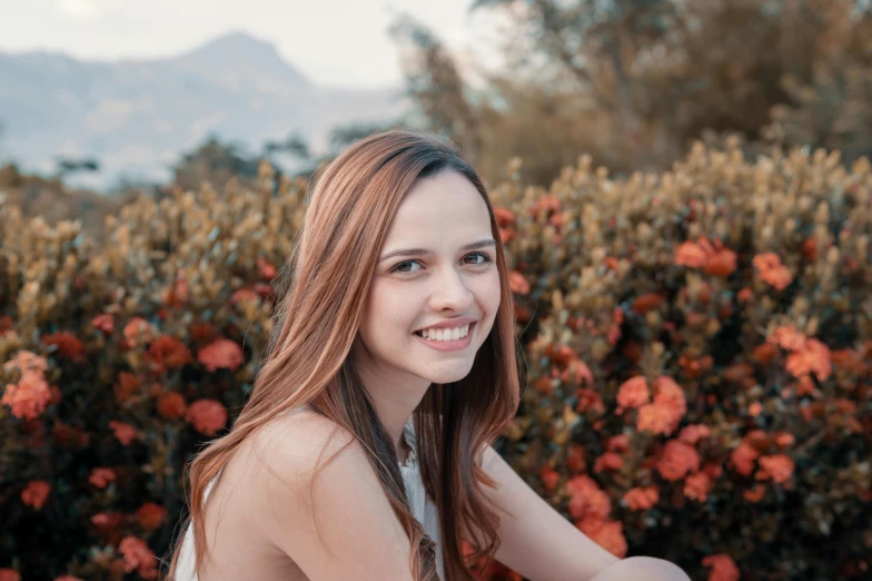 a woman is smiling and sitting in front of some bushes