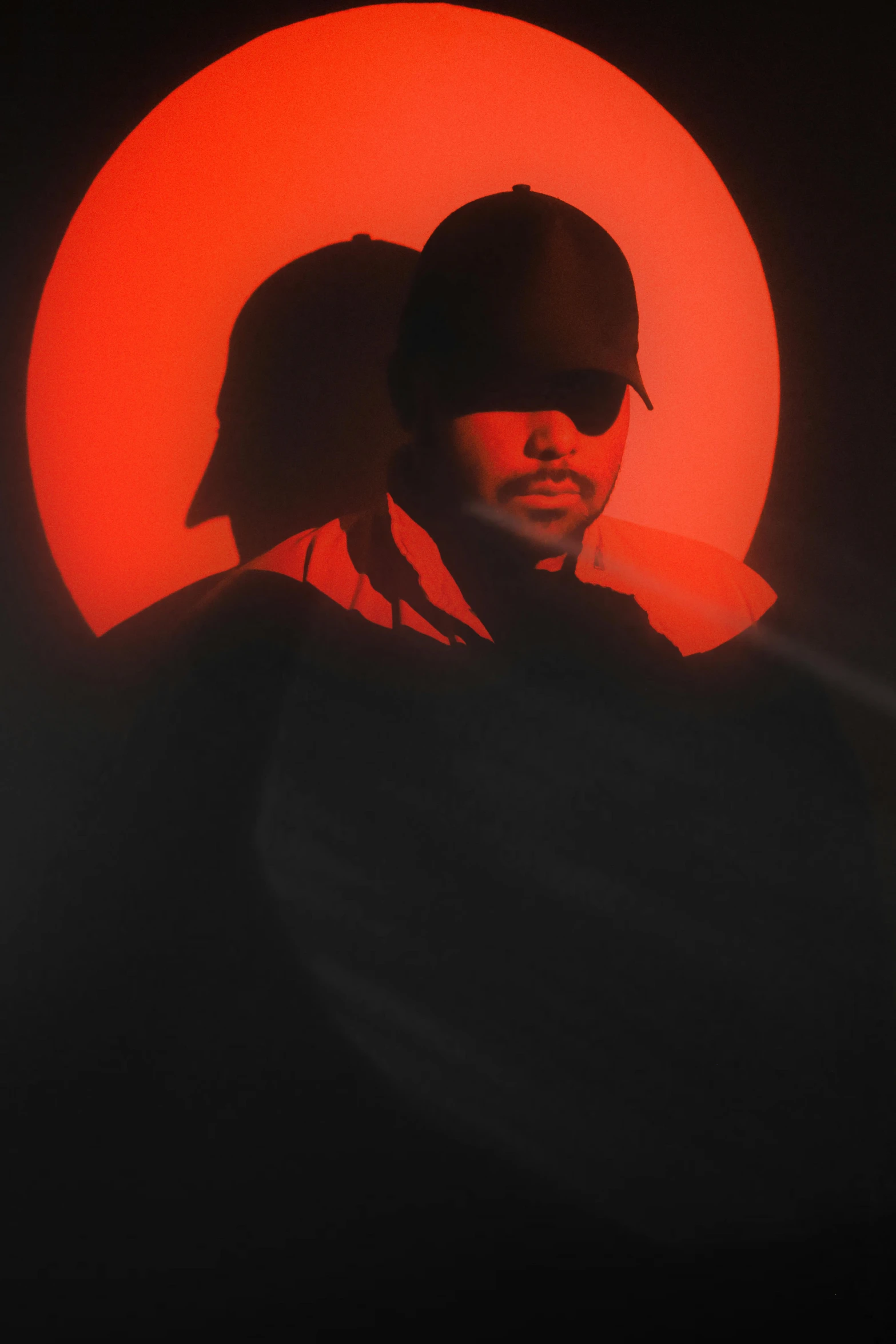 a man in a hat stands in the dark with an orange circle behind him