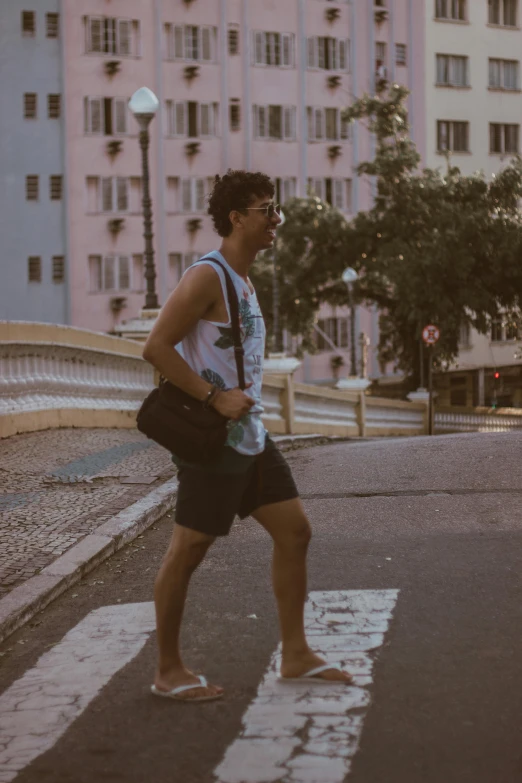 man in sandals walking across a street next to buildings