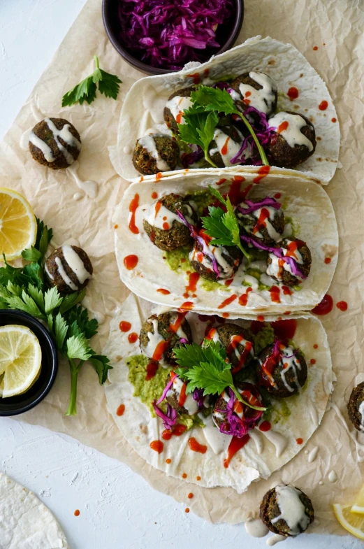 several tacos on parchment paper with lime wedges, and red cabbage salad