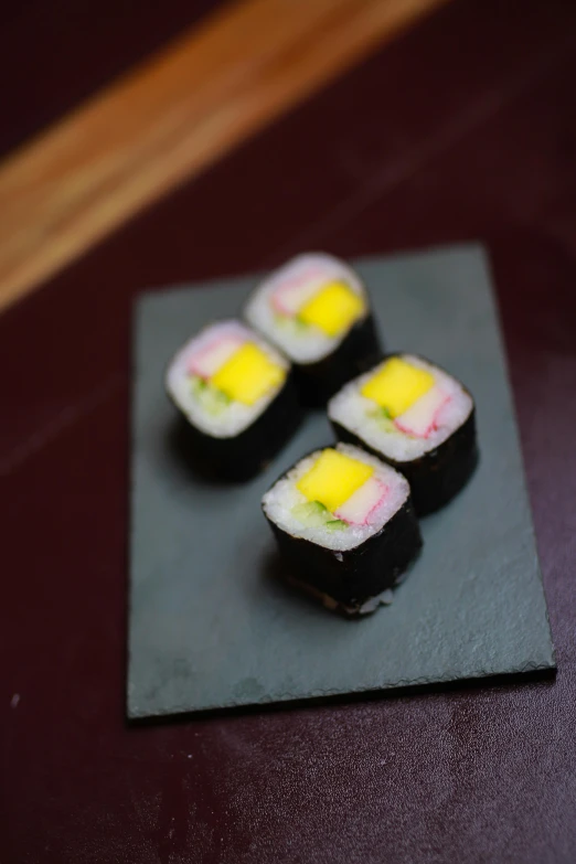 some pieces of sushi with yellow on a small square plate