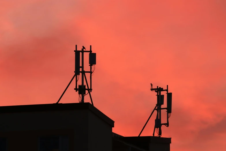 two cellular towers silhouetted against a red sky