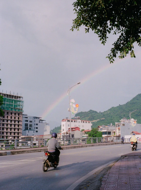 people on motorcycles driving on an urban street with a rainbow in the sky