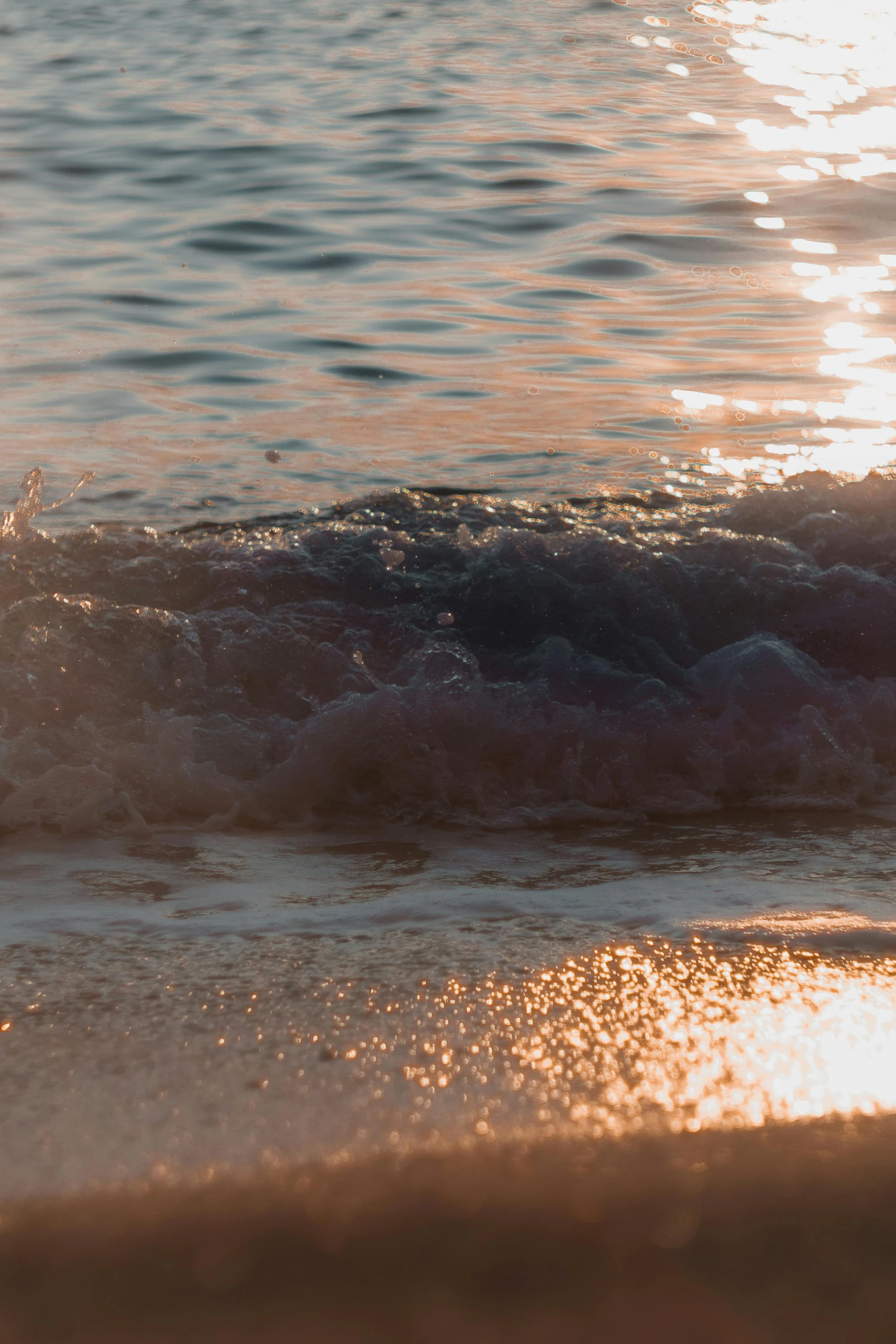 water splashes onto a beach as the sun is setting