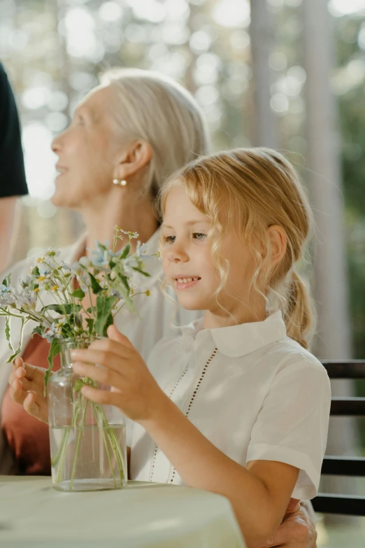 an older lady and  smiling behind a vase with some flowers