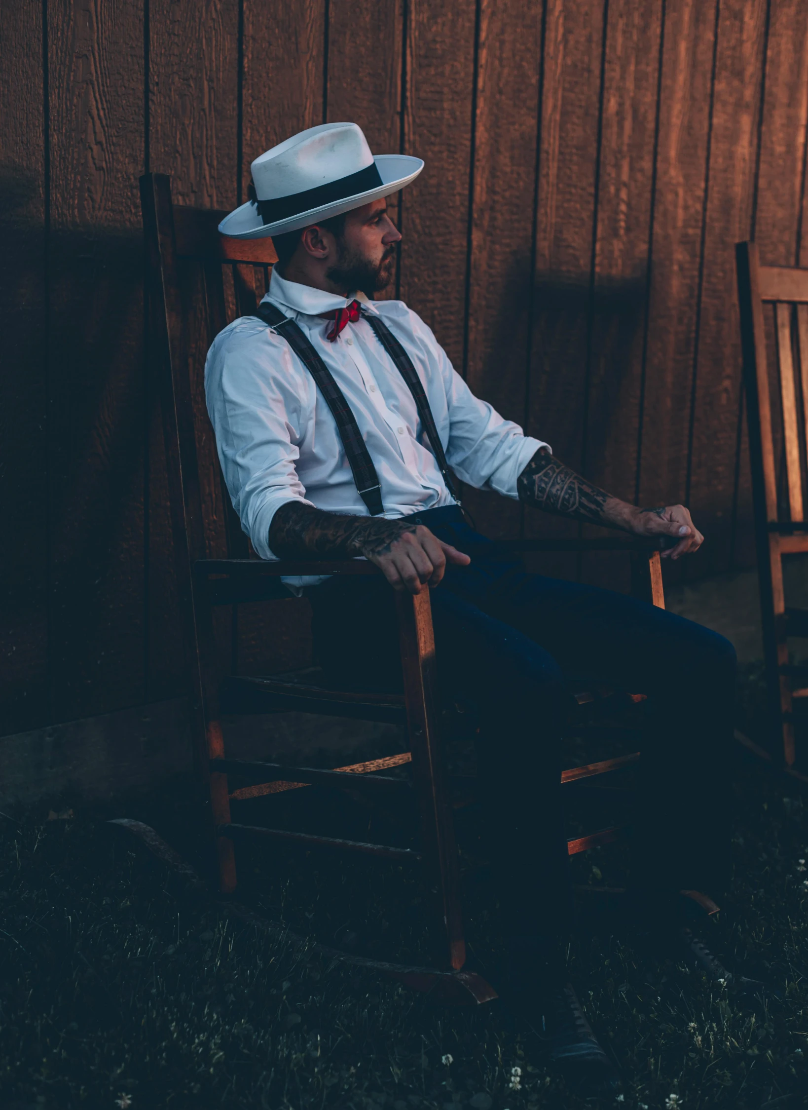 a man in suspenders sitting on a wooden chair