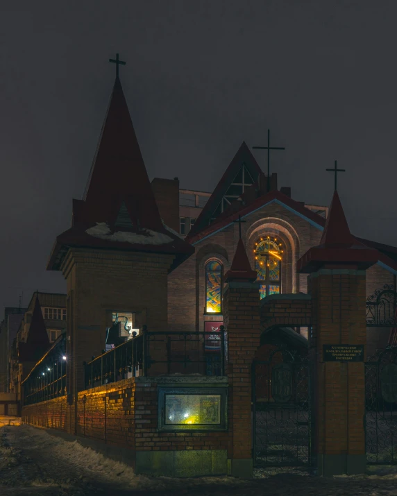 a church with a gate, steeple and stained glass window at night
