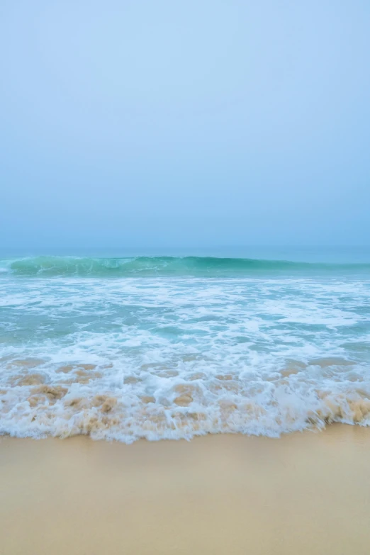 the ocean waves are crashing on to a sandy beach