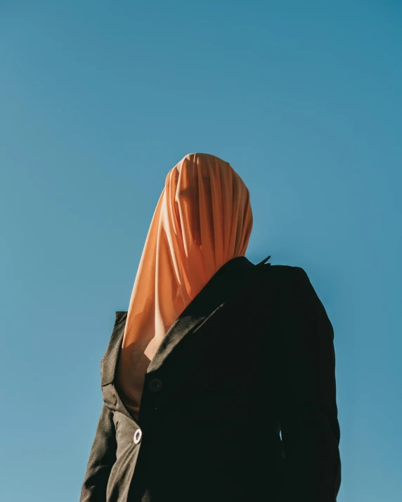 a person with an orange sheet on their head standing next to a building