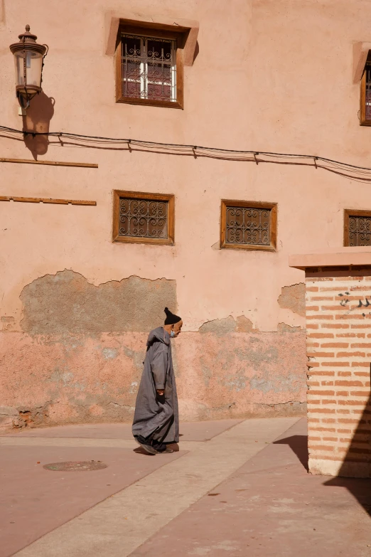 an older person wearing a gray cloak and shoes walking along a sidewalk