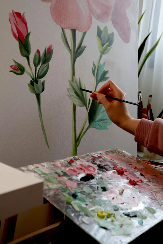 a woman paints on a flowered wall with acrylic paint