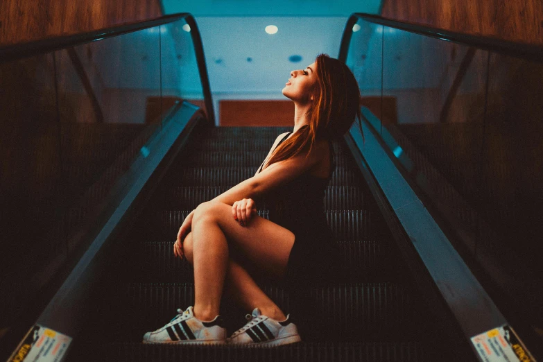 woman in a brown dress and blue sneakers is sitting on the escalator