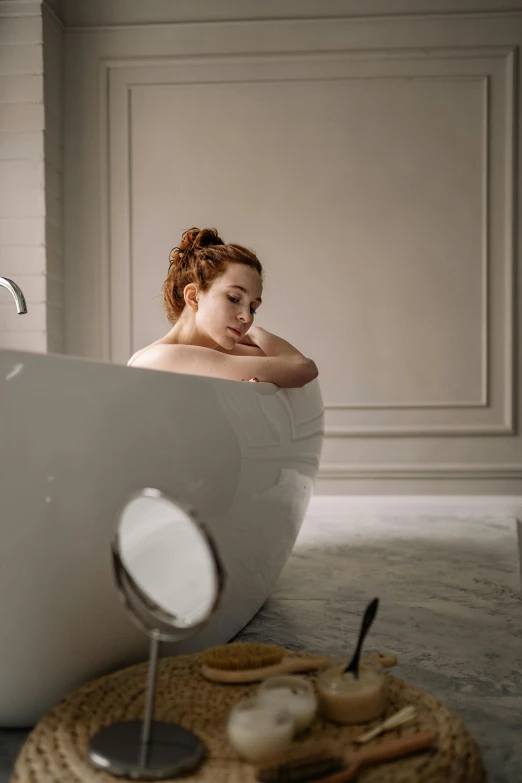 a woman is sitting in a bathtub with a knife and small mirror nearby