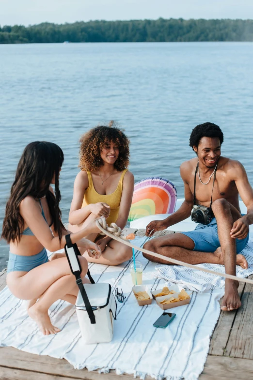 group of people sitting on dock next to lake eating