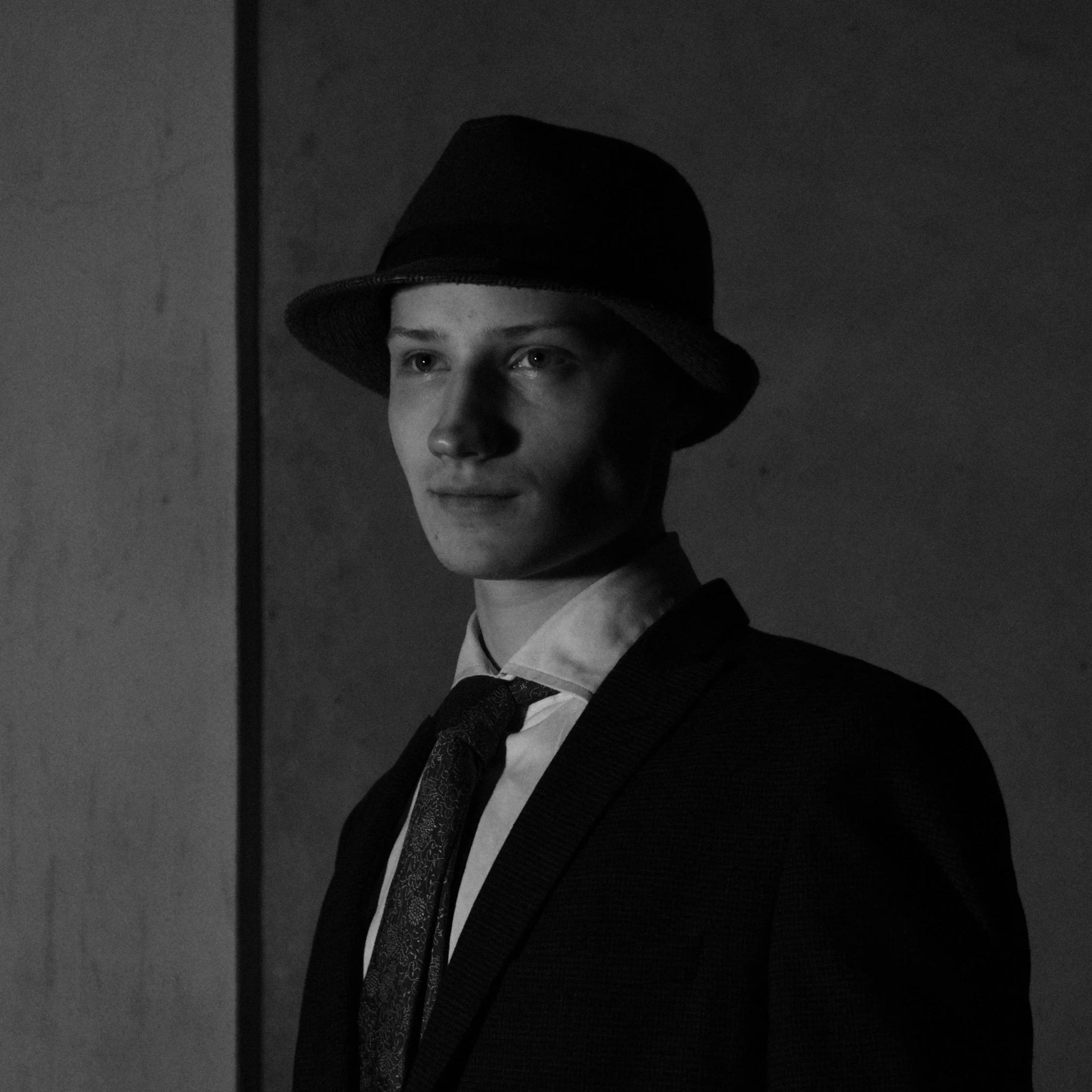 a man with a hat and tie standing by a wall