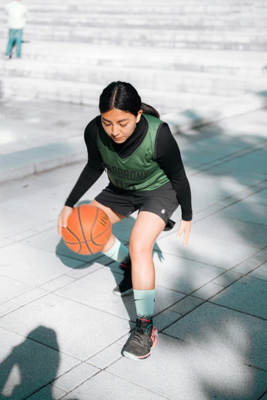 woman holding a basketball on a sidewalk and crouching