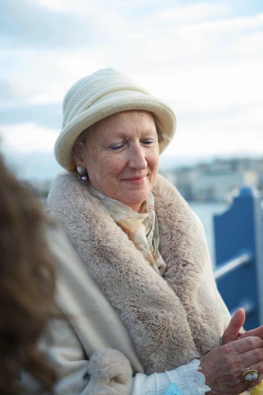 a woman in beige and a tan coat with a beige shawl is talking to a lady outside