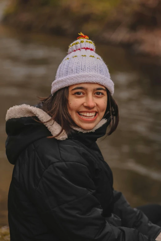 a smiling woman wearing a hat is sitting by the water