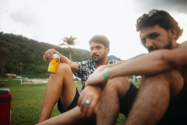 two men sitting down near a cooler bottle on the ground