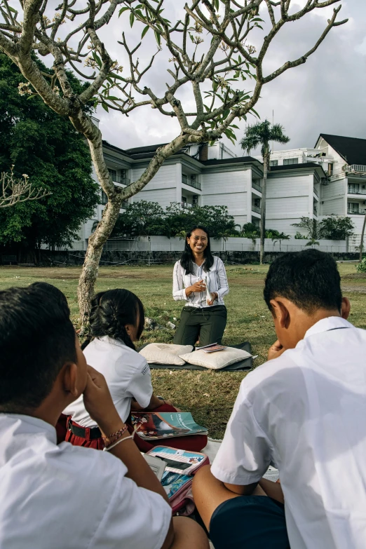 a woman sitting down talking to children in the grass