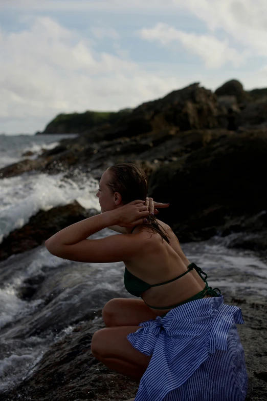 a young woman crouching on rocks next to the ocean