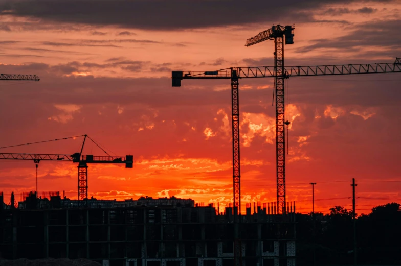 the sun is setting over the skyline while construction cranes stand tall