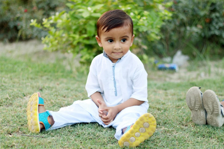 a little boy sitting in the grass next to some shoes