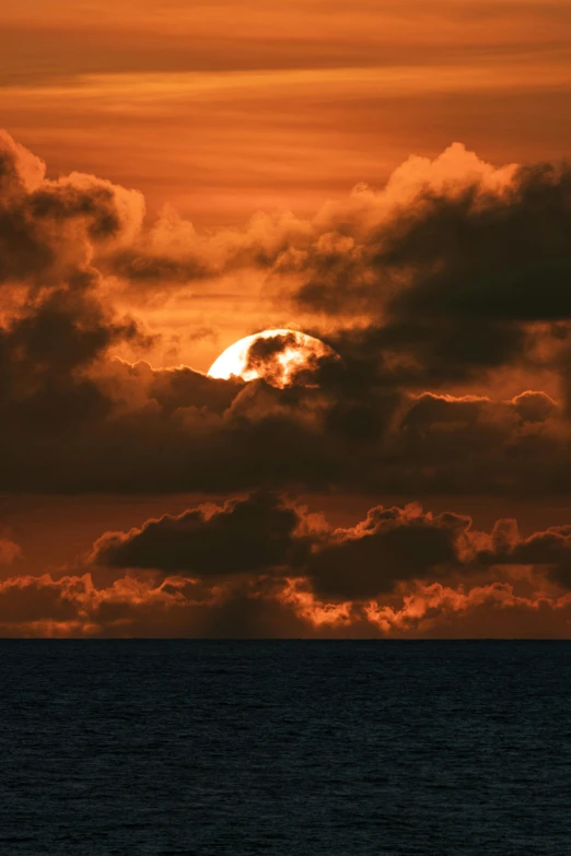 a sail boat in the ocean and a large sun behind it