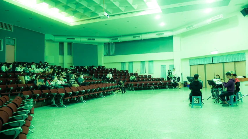 two men sit in rows on red chairs in an empty lecture hall