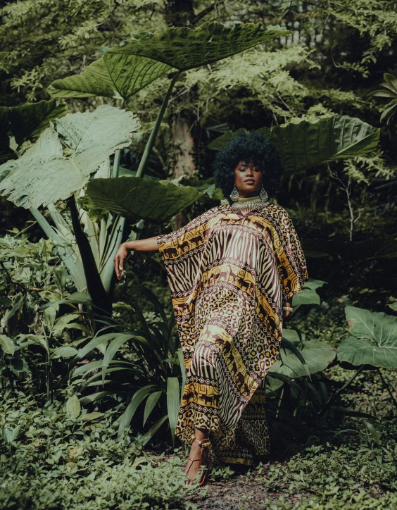 a young woman wearing a yellow and black print shirt standing in a green jungle