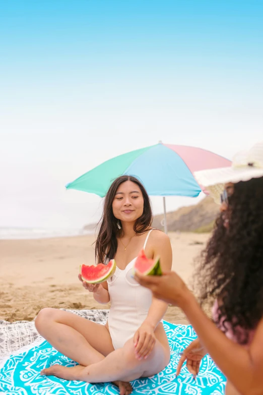 a woman sitting on the beach eating a watermelon