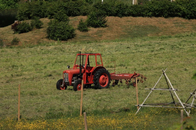 a red tractor in a field next to an unfinished trellis