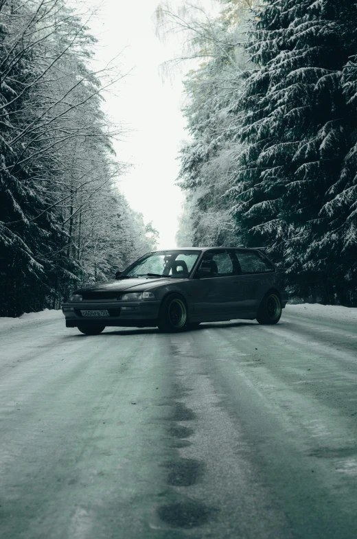 black car on snowy road with trees and sun peeking out from the window