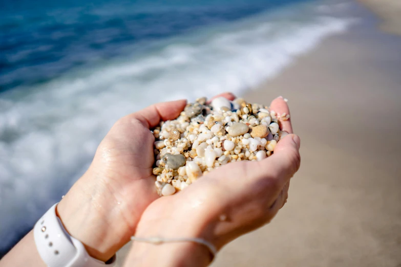 a person holding small pebbles on the beach