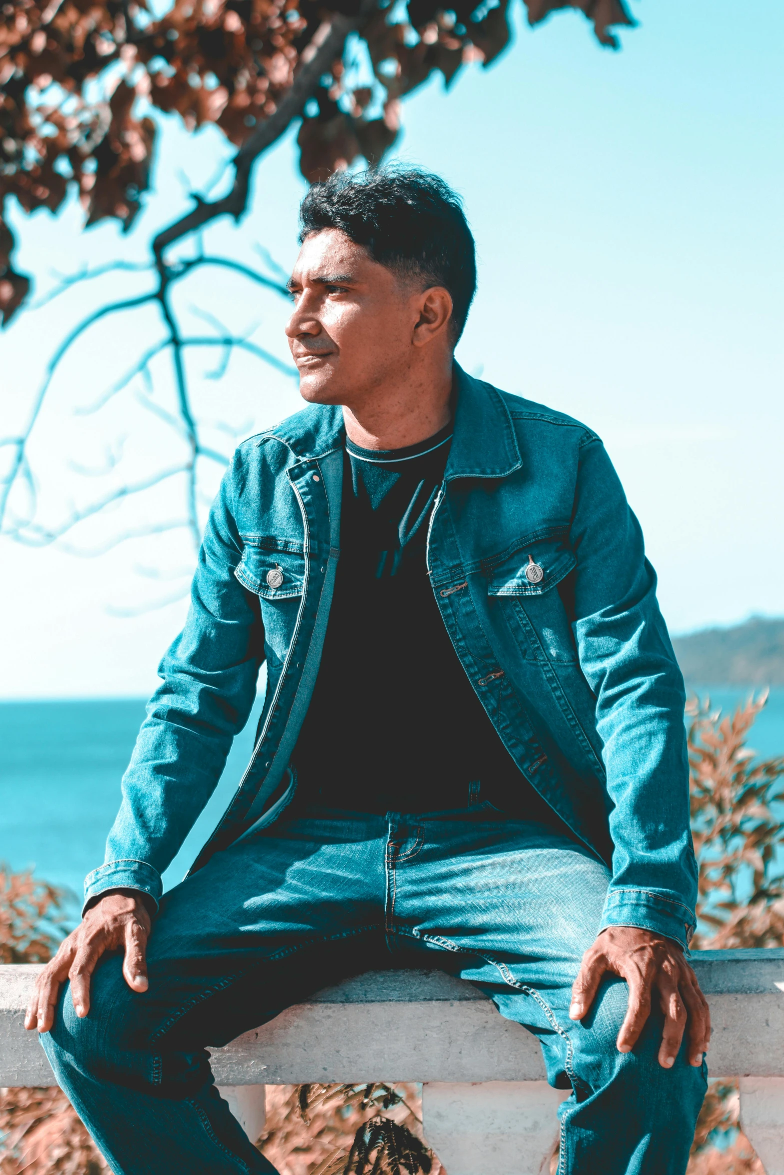 a man wearing jeans sits outside on a balcony