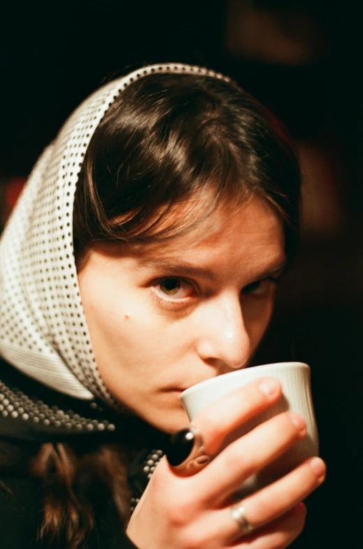 a young woman with a scarf and head covering drinking from a mug