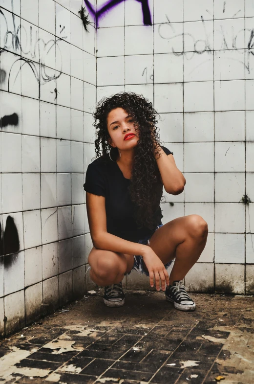 a beautiful young lady squatting against a wall